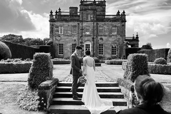 Black and white image of bride and groom walking up steps in front of country house venue